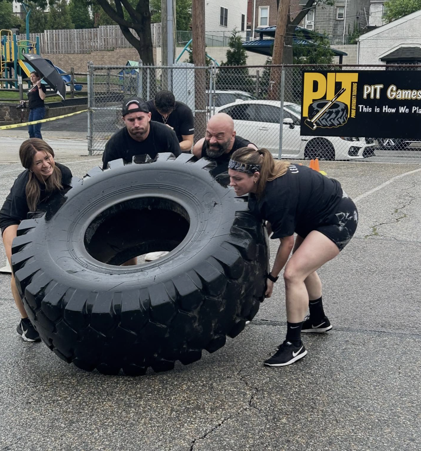 Group of four people outdoors at Prime Intensity Training in Ambler, Pennsylvania, working together to flip a large tractor tire during a fitness challenge event